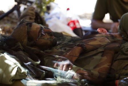 An Israeli soldier covered in camouflage netting rests at a military staging area outside the Gaza Strip July 23, 2014. Israeli forces pounded Gaza on Wednesday, meeting stiff resistance from Hamas Islamists and sending thousands of residents fleeing, as U.S. Secretary of State John Kerry said on a visit to Israel ceasefire talks had made some progress. REUTERS/Ronen Zvulun