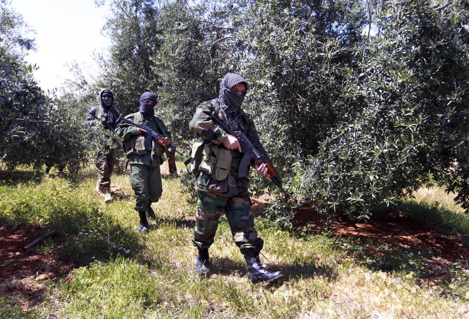 In this Friday, April 12, 2013 photo, Hezbollah fighters walk through a field at the Lebanon-Syria border, near the northeastern Lebanese town of al-Qasr, Lebanon. The Shiite group has sent hundreds of its fighters into Syria to shore up President Bashar Assad’s overstretched troops, helping them gain ground around the capital, Damascus, and near the Lebanese border. But with its own casualties mounting in a civil war that activists say has killed more than 150,000 people in three years, officials say Hezbollah has turned to a variety of new tactics - including complicated commando operations - to hunt down rebels and opposition commanders. (AP Photo/Bilal Hussein)