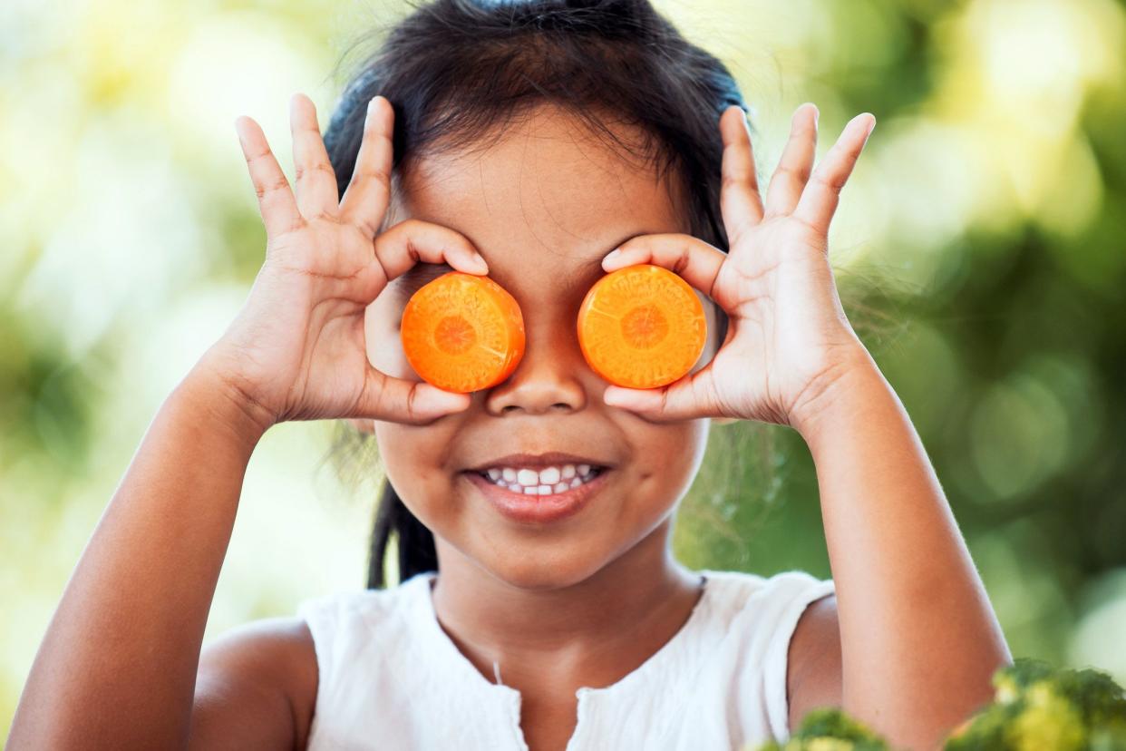 little girl holding up carrot slices over her eyes and smiling