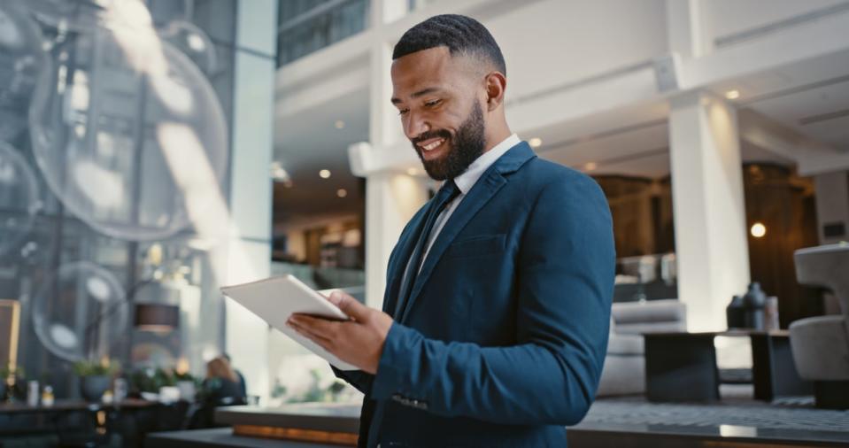 A person dressed in formal attire smiles while interacting with a tablet. 