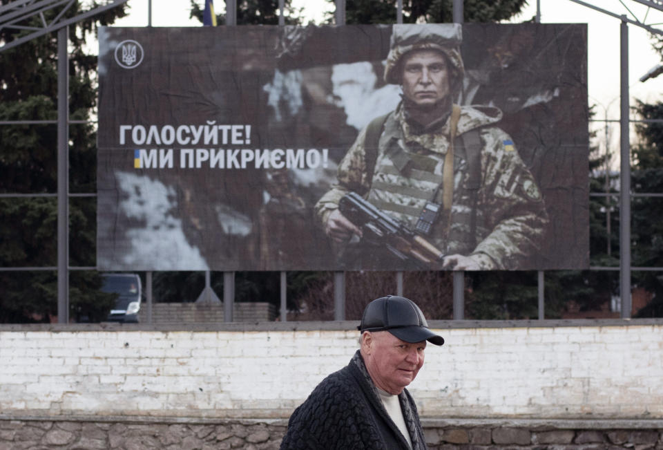 A local man walks past an election poster depicting a Ukrainian soldier with a sign reading 'Go for vote, we protect you,' during the president elections in Mariinka, near a contact line not far from Donetsk, eastern Ukraine, Sunday, March 31, 2019. The exit poll released Sunday after voting stations closed indicated that Zelenskiy received about 30.4 percent of the nationwide vote, followed by incumbent President Petro Poroshenko with 17.8 percent and former Prime Minister Yulia Tymoshenko with 14.2 percent support. (AP Photo/Evgeniy Maloletka)