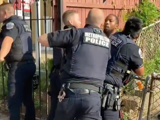 A DC Metropolitan Police Officer pulls back to punch a Black man who is restrained by other officers.  (screengrab)