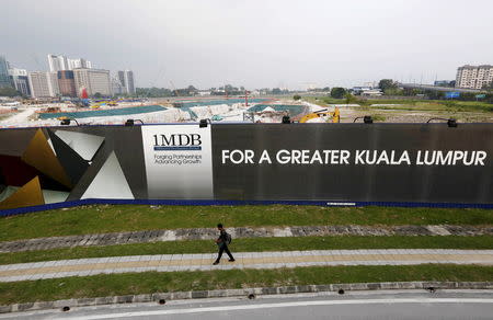 FILE PHOTO: A man walks past a 1 Malaysia Development Berhad (1MDB) billboard at the funds flagship Tun Razak Exchange development in Kuala Lumpur, March 1, 2015. REUTERS/Olivia Harris/File Photo