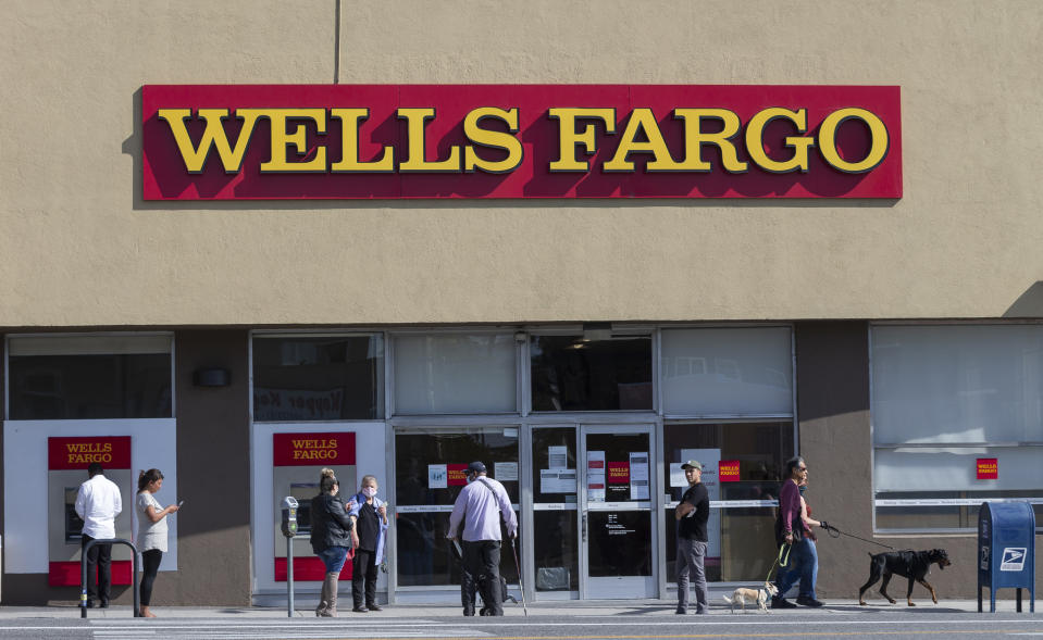 FILE - In this April 3, 2020, file photo, customers, some wearing face masks, line up outside a Wells Fargo branch in the Atwater Village neighborhood of Los Angeles, during the coronavirus outbreak. Wells Fargo, on Tuesday, July 14, says it lost $2.4 billion in the second quarter, the first quarterly loss for the bank since the real estate crash of 2008. (AP Photo/Damian Dovarganes, File)