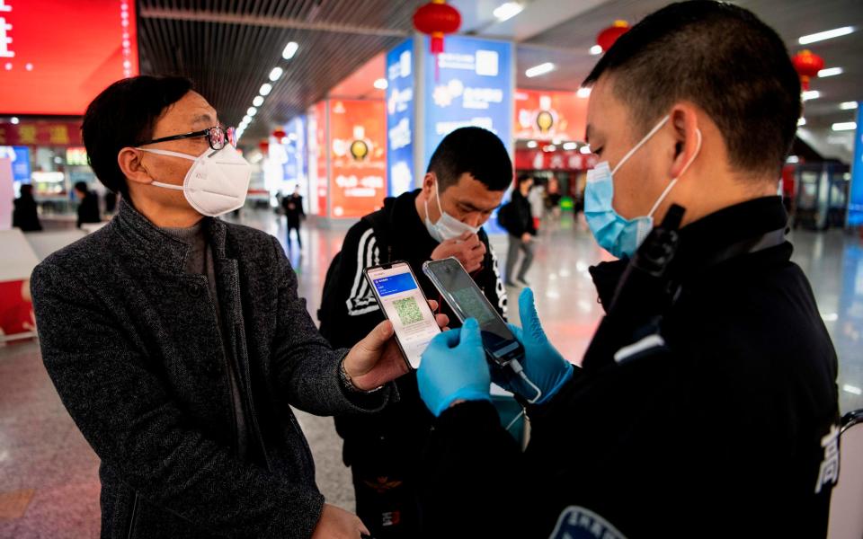 A passenger wearing a face mask as he shows a green QR code on his phone to show his health status to security upon arrival at Wenzhou railway station in Wenzhou, China - NOEL CELIS /AFP