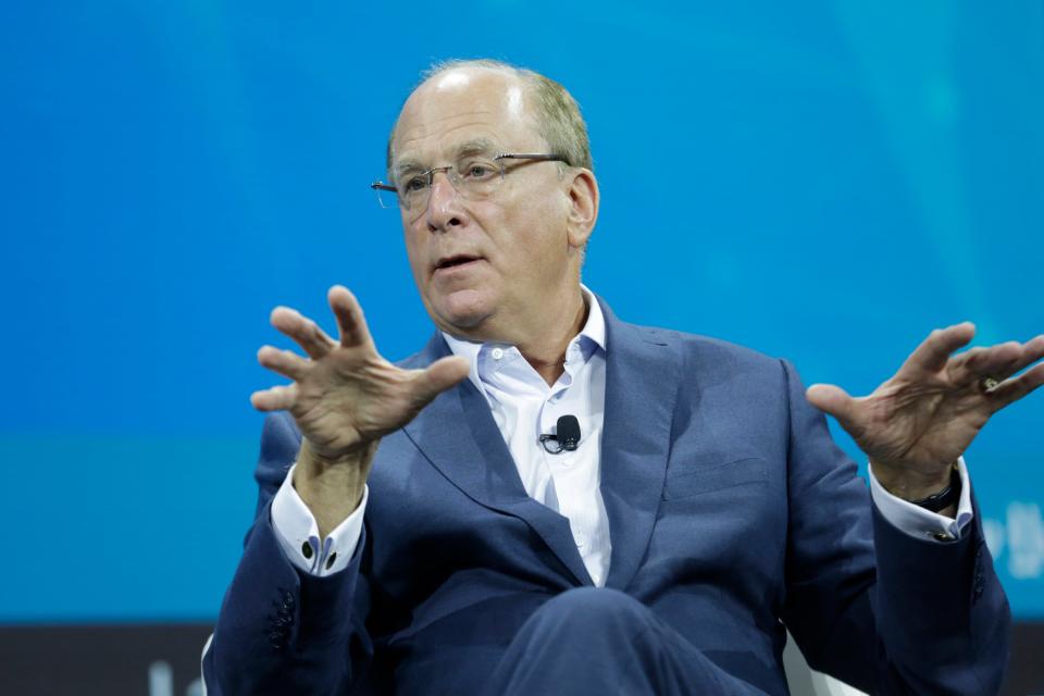 BlackRock CEO Larry Fink gestures while sitting in front of a blue screen.