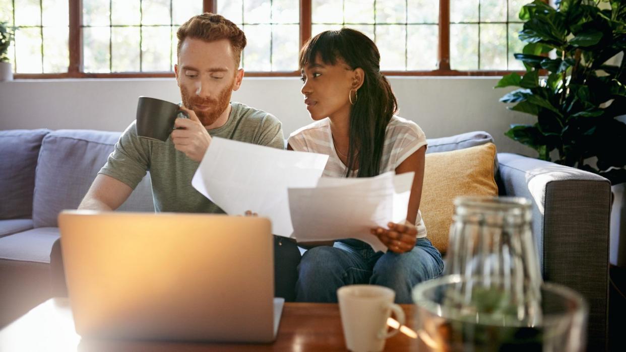 Shot of a young couple going through paperwork while using a laptop at home.