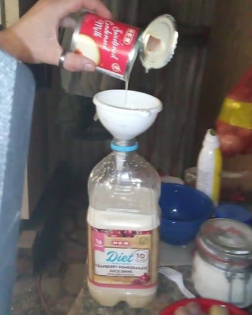 someone pouring condensed milk through a funnel into a plastic bottle