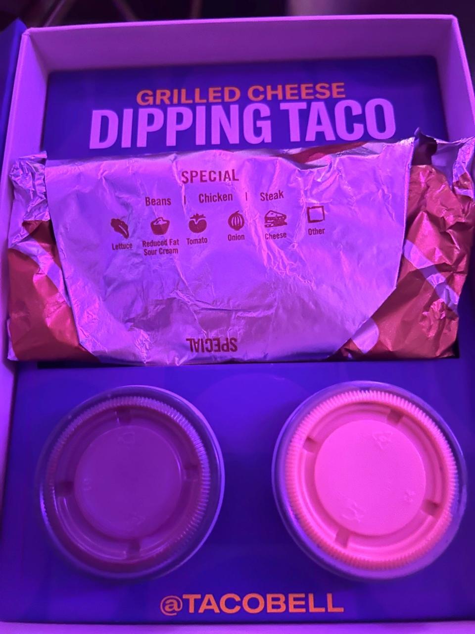 A Taco Bell box containing a Grilled Cheese Dipping Taco with a pot of red sauce and a pot of nacho-cheese sauce