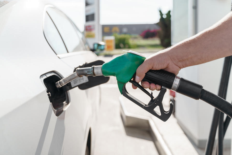 A close-up of a person's hand holding a fuel pump nozzle, refueling a car at a gas station