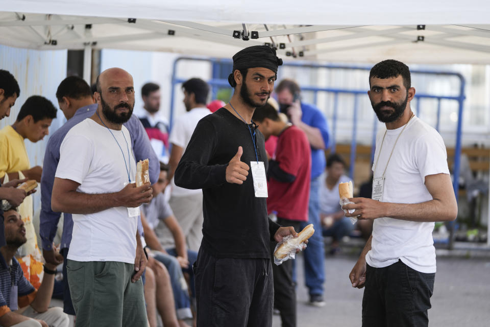 Survivors of a shipwreck eat outside a warehouse at the port in Kalamata town, about 240 kilometers (150miles) southwest of Athens, on Thursday, June 15, 2023. A fishing boat crammed to the gunwales with migrants trying to reach Europe capsized and sank Wednesday off the coast of Greece, authorities said, killing and missing multiple people in one of the worst disasters of its kind this year. (AP Photos/Thanassis Stavrakis)