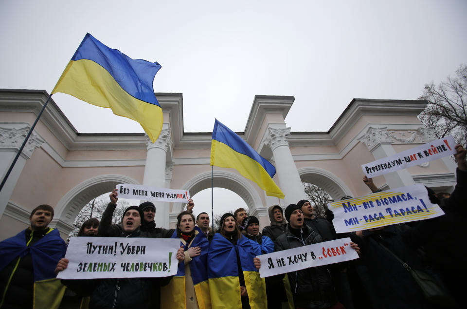 People hold Ukrainian flags and banners that read: "Putin! Take away the green men", "They got me married without me being there", "Referendum is a step to war", during a rally against the breakup of the country in Simferopol, Crimea, Ukraine, Tuesday, March 11, 2014. The Crimean parliament voted Tuesday that the Black Sea peninsula will declare itself an independent state if its residents agree to split off from Ukraine and join Russia in a referendum. Crimea's regional legislature on Tuesday adopted a "declaration of independence of the Autonomous Republic of Crimea." The document specified that Crimea will become an independent state if its residents vote on Sunday in favor of joining Russia in the referendum. (AP Photo/Darko Vojinovic)