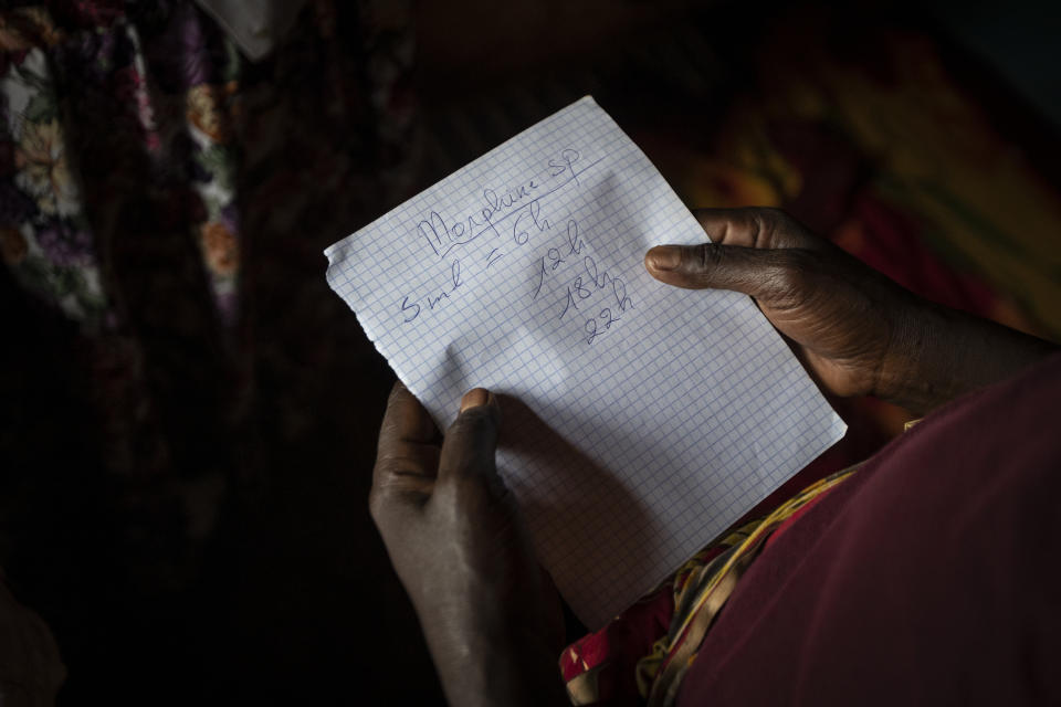 In this photo taken Monday, Nov. 4, 2019, Maria Mukamabano holds a handwritten note advising the schedule that her mother-in-law and cancer patient Athanasie Nyirangirababyeyi, 89, should take her oral liquid morphine for her pain, during a visit to check on her health by palliative care nurse Madeleine Mukantagara at her son's home in the village of Kagano, near Kibogora, in western Rwanda. While people in rich countries are dying from overuse of prescription painkillers, people in Rwanda and other poor countries are suffering from a lack of them, but Rwanda has come up with a solution to its pain crisis - it's morphine, which costs just pennies to produce and is delivered to households across the country by public health workers. (AP Photo/Ben Curtis)