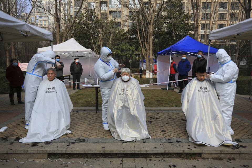 Hairdressers wearing protected suits cut residents' hair at a residential block which has become under lockdown in Xi'an in northwest China's Shaanxi province on Sunday, Jan. 9, 2022. A major Chinese city near Beijing has placed its 14 million residents on partial lockdown after a number of children and adults tested positive for COVID-19, including at least two with the omicron variant. Elsewhere, millions of people are being confined to their homes in Xi'an and Yuzhou, two cities that are farther away but have larger outbreaks traced to the delta variant. (Chinatopix Via AP)