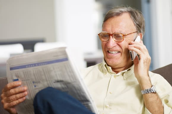 Older man squinting at a newspaper and talking on the phone