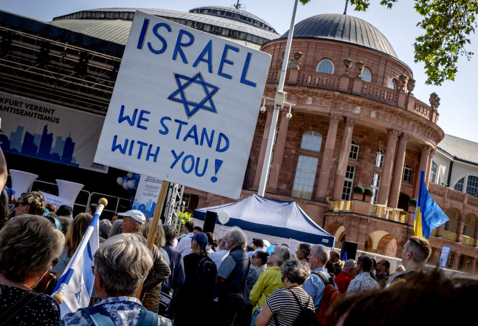 A woman holds a sign as she takes part in a demonstration against a concert later the day of former Pink Floyd musician Roger Waters in the Festhalle, background, in Frankfurt, Germany, Sunday, May 28, 2023. The Festhalle was the place where in the night of broken glasses 1938 about 3000 Jewish men where gathered to deport them to concentration camps. (AP Photo/Michael Probst)