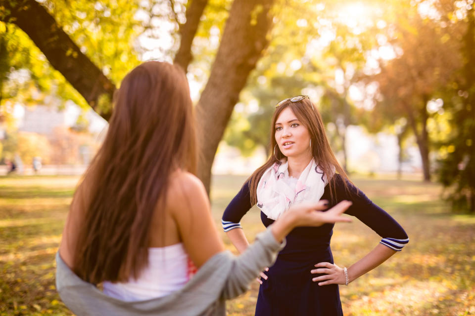 Two women talking in a park, one with hands on her hips, likely discussing wedding plans