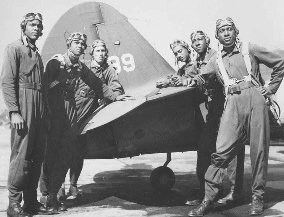 A number of men in pilot uniforms stand beside a plane