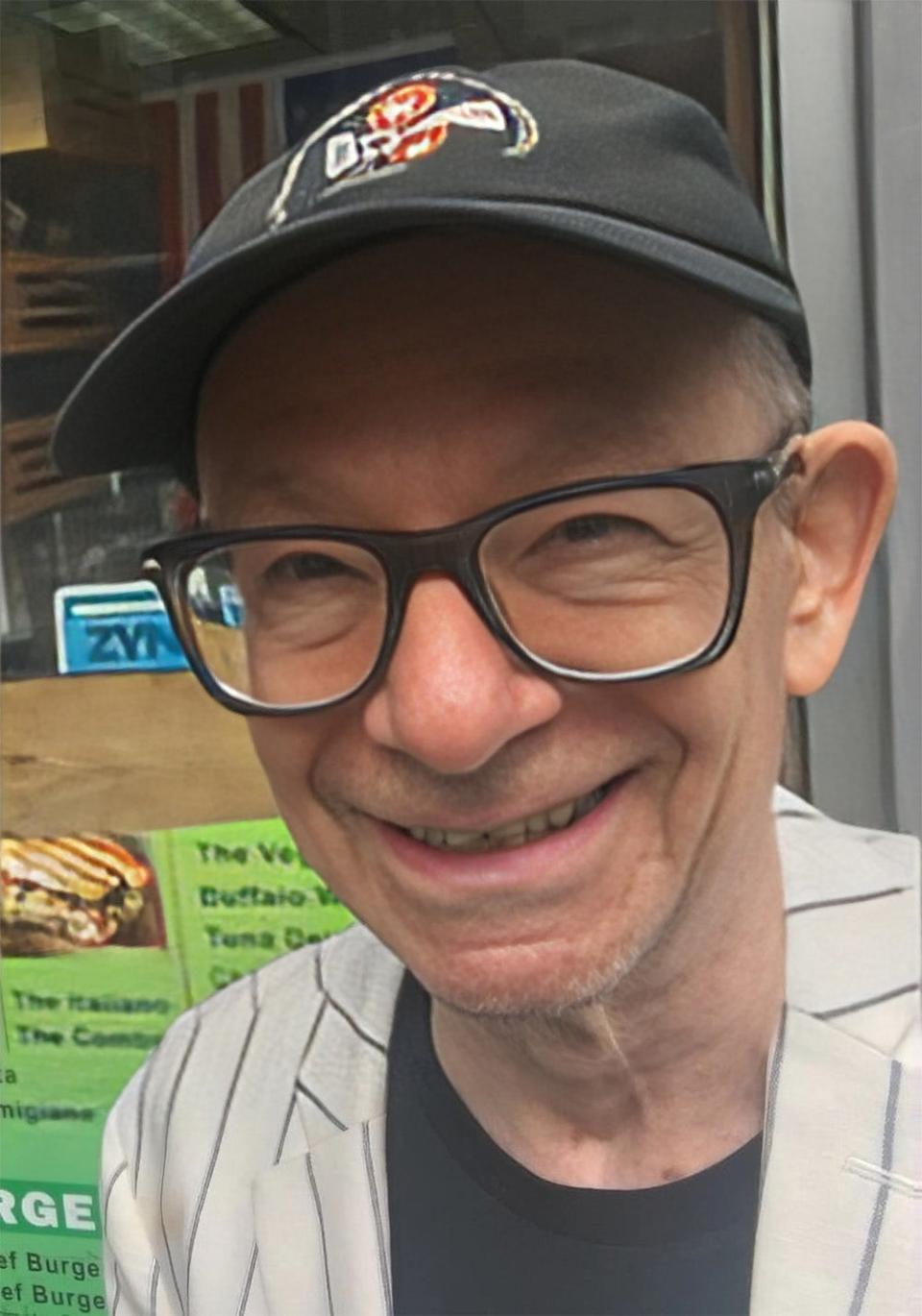 A close-up of John Meyer smiling wearing glasses and a hat