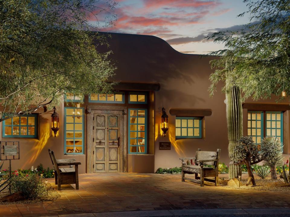 An adobe building with two benches out front and a cloudy sunset in the background