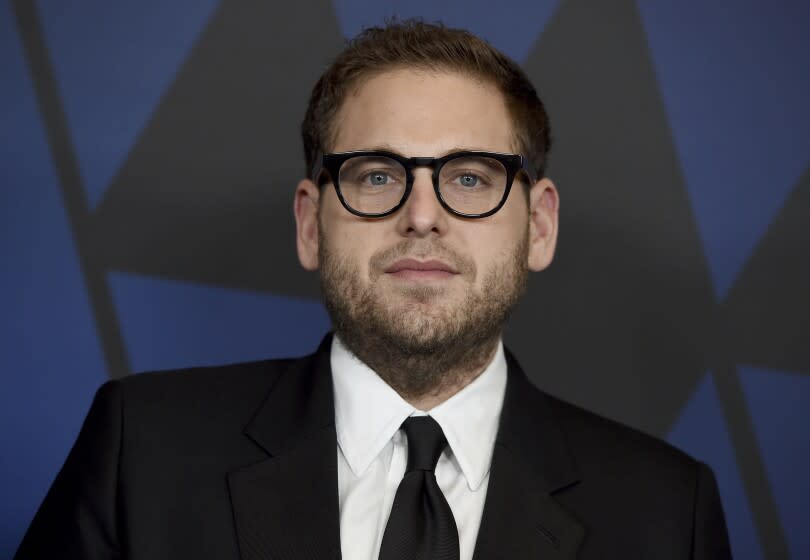 A young man wearing black-rimmed eyeglasses and a black suit