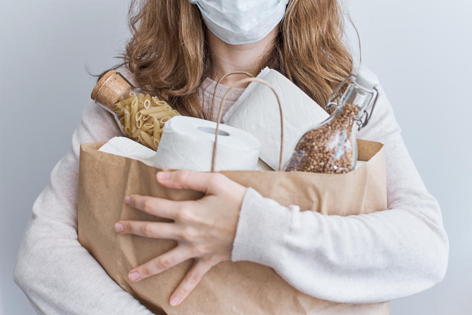 Consumer buying panic about coronavirus covid-19 concept. People buy essentials in bulk at supermarkets concept. Woman hold shopping bag with rolls of toilet paper, pasta and buckweat