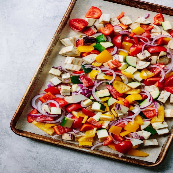 Lots of diced vegetables including pepper, zucchini, and red onion on a sheet pan.