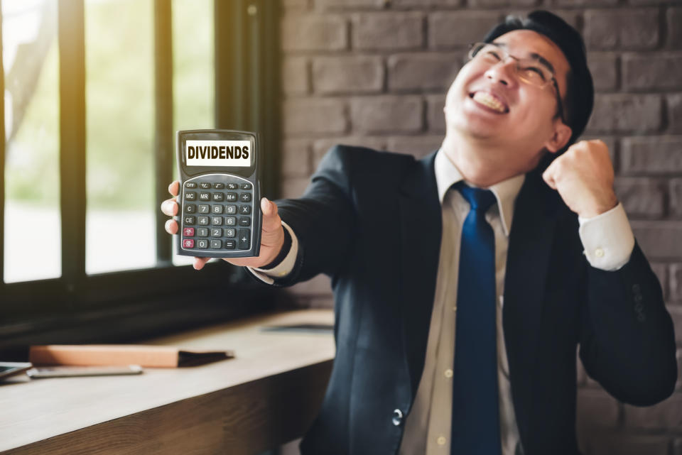 A cheering man holding a calculator with the word 'dividends' on the screen