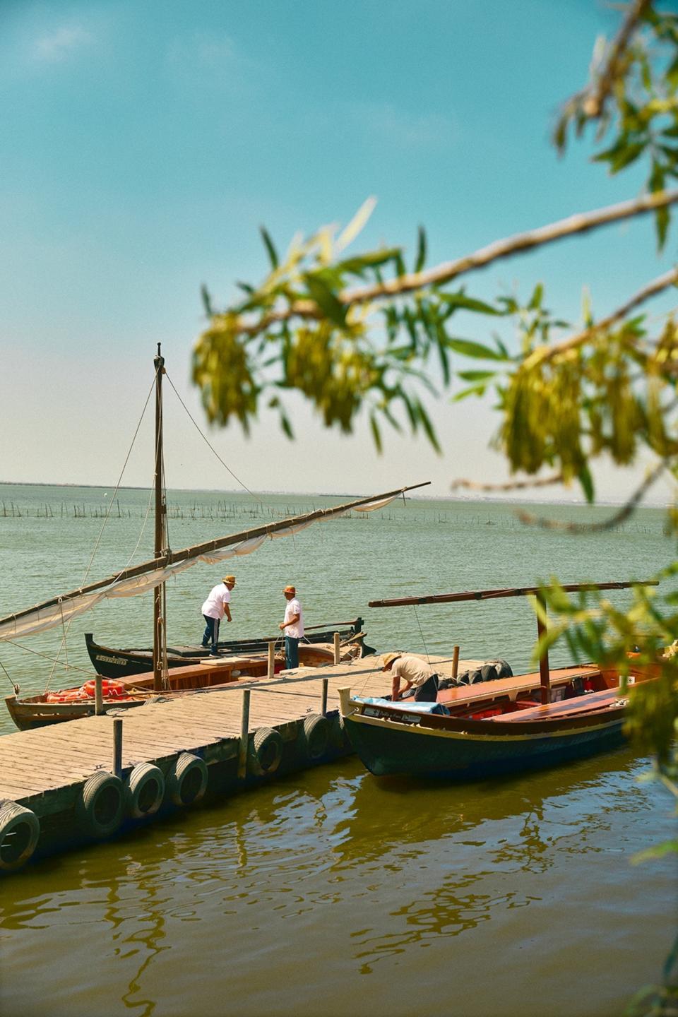 Men stand in wooden boats at a jetty on a lagoon