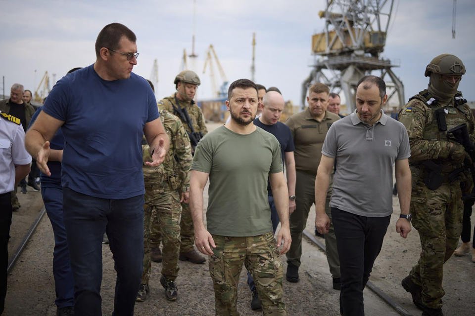 In this photo provided by the Ukrainian Presidential Press Office, Ukrainian President Volodymyr Zelenskyy, center, surrounded by ambassadors of different countries and UN officials, visits a port in Chornomork during loading of grain on a Turkish ship, background, close to Odesa, Ukraine, Friday, July 29, 2022. (Ukrainian Presidential Press Office via AP)