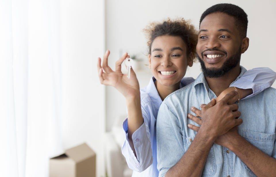 Joyful African American Couple Holding Key Embracing Standing In New Flat After Moving. Selective Focus, Copy Space