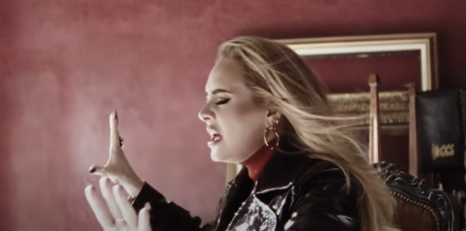 Adele in profile, gesturing expressively, with hoop earrings and a leather jacket
