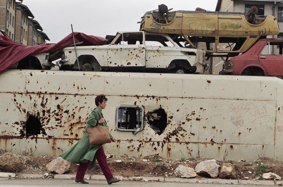 <p>A Bosnian woman walks next to a barricade made of mortar and bullet-damaged buses and cars as she makes her way through the frontline neighborhood of Dobrinja in Sarajevo, Nov. 13, 1994. (Photo: Jacqueline Larma/AP) </p>