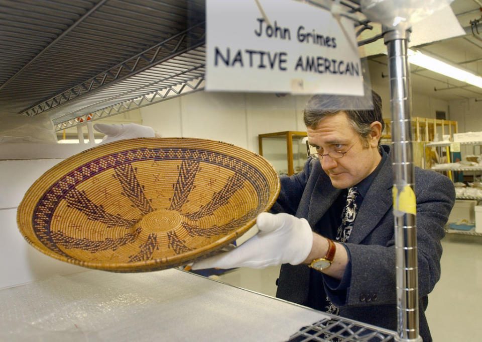 Person examining a Native American woven basket; sign reads 'John Grimes NATIVE AMERICAN'
