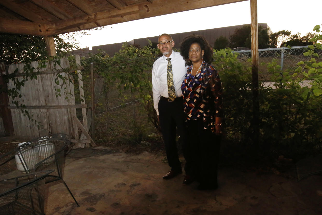 Frank and Michelle Meeks stand in their backyard in Arlington, Texas, on Sunday, Oct. 24, 2021, with a fracking site, hidden by "sound walls," looming behind them. The site, called "Rocking Horse," is operated by TEP Barnett, a subsidiary of French energy giant Total Energies and is just a few hundred feet from their home. Beyond concerns about long-term health risks posed by fracking, the Meeks say they've endured frequent drilling noise and vibration in recent months. They and other neighbors also say the drilling has damaged their homes' foundations. (AP Photo/Martha Irvine)