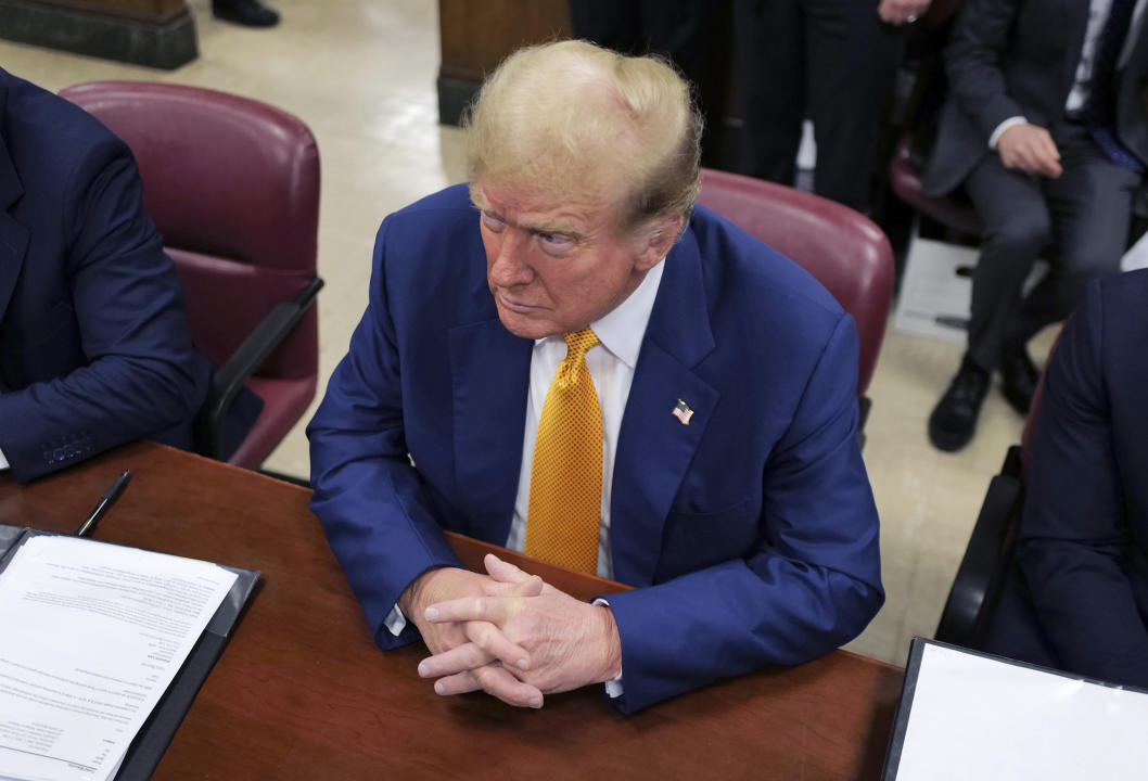 From above, Trump seated at a table with his hands clasped.