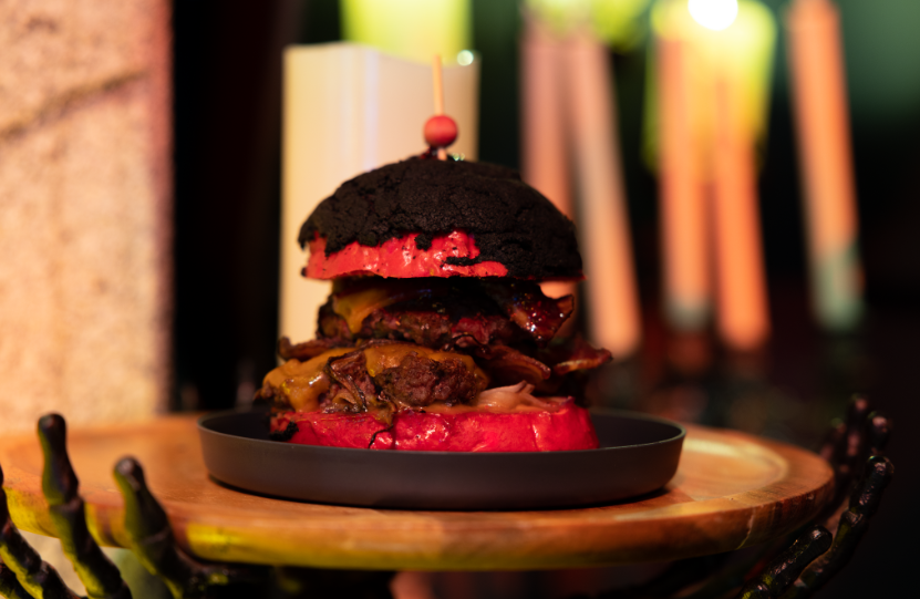 The Peanut Blooder Burger featured at Universal Orlando's Taste of Terror for Halloween Horror Nights. It is a slider with peanut sauce, raspberry jelly, cheddar, jalapeño, bacon and cherry peppers on a black bun.