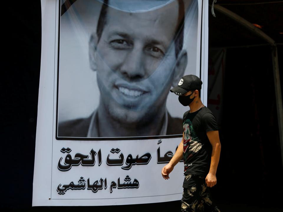 A protestor walks by poster of Hisham al Hashimi