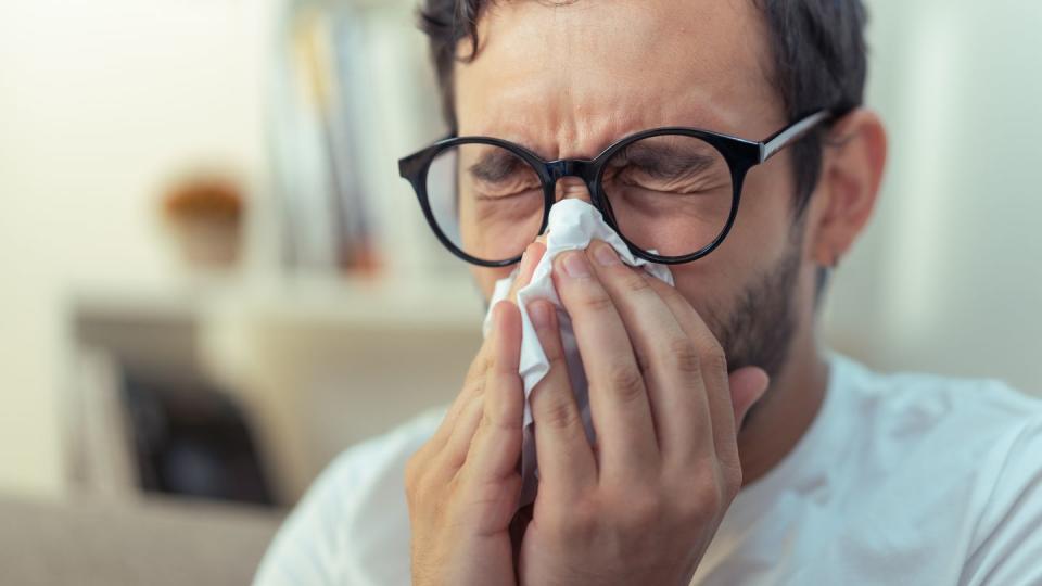 young man sneezing, wiping his nose with a piece of tissue paper