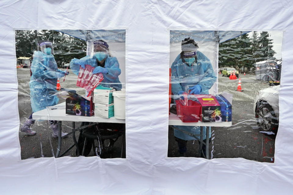 FILE - Workers at a drive-up COVID-19 testing clinic stand in a tent as they prepare PCR coronavirus tests, Jan. 4, 2022, in Puyallup, Wash., south of Seattle. Scientists are seeing signals that COVID-19′s alarming omicron wave may have peaked in Britain and is about to do the same in the U.S., at which point cases may start dropping off dramatically. (AP Photo/Ted S. Warren, File)