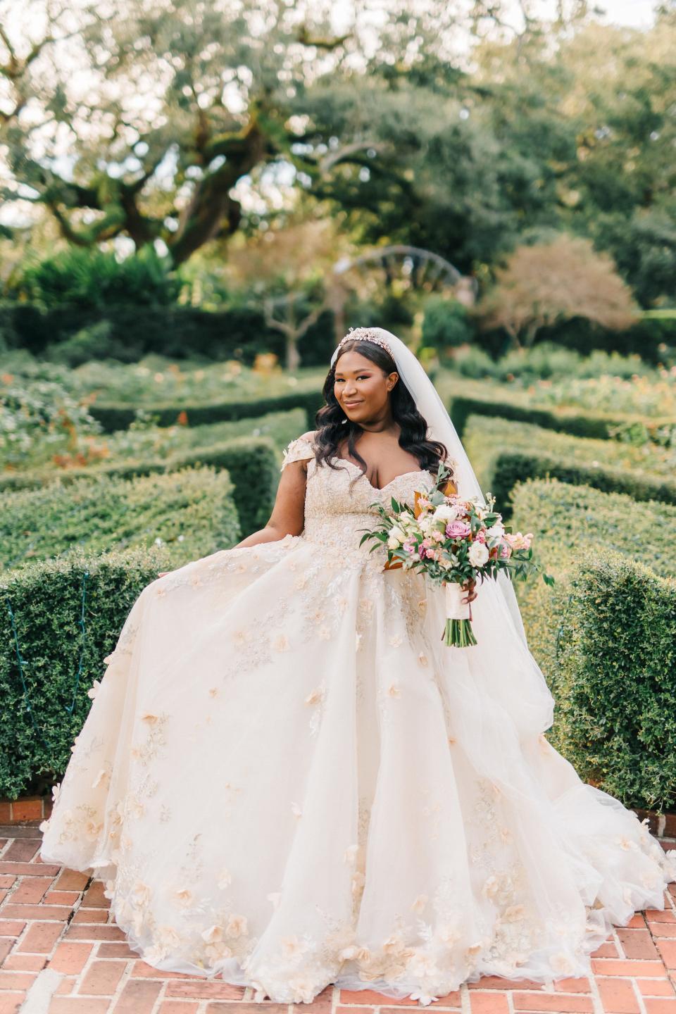 A bride poses in her wedding dress in front of greenery.