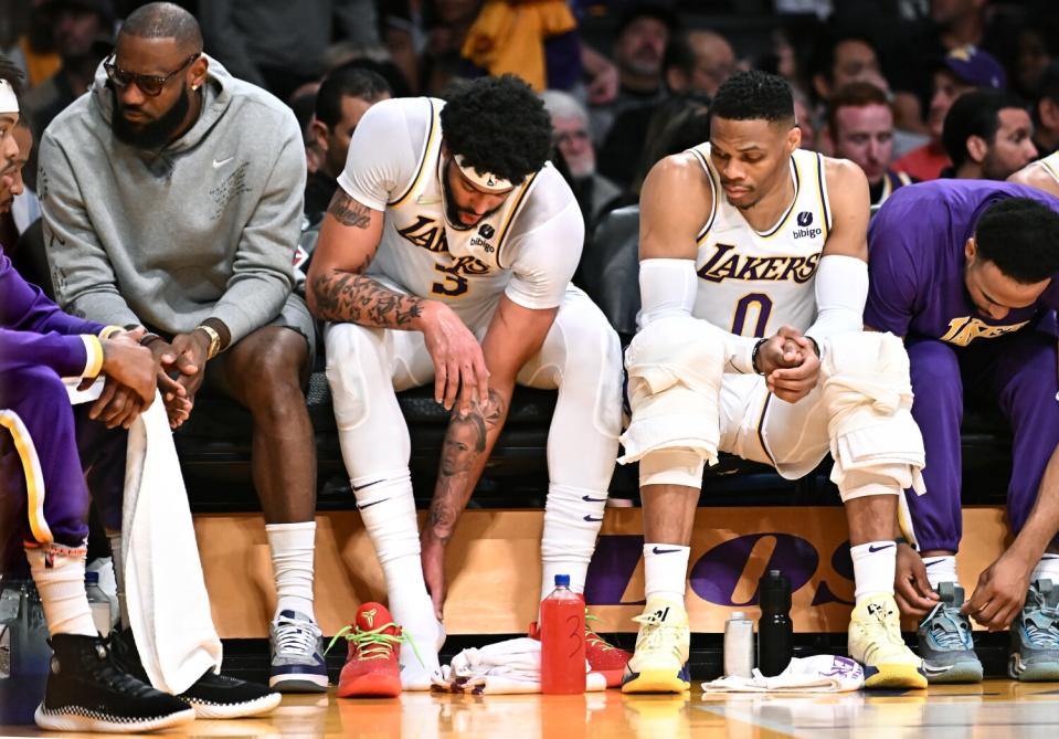 Anthony Davis, center, holds his ankle as he's flanked on the bench by an injured LeBron James, left, and Russell Westbrook.