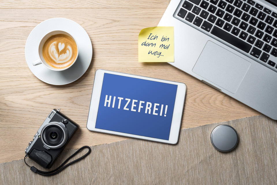 Hitzefrei written in german on tablet meaning having time off from work or school on account of excessively hot weather or heat wave and I'm gone on sticky note as flatlay from above of an office desk