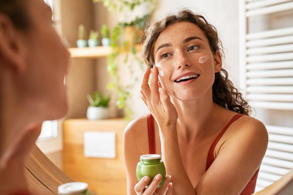 A person smiling while looking in the mirror and applying face cream.