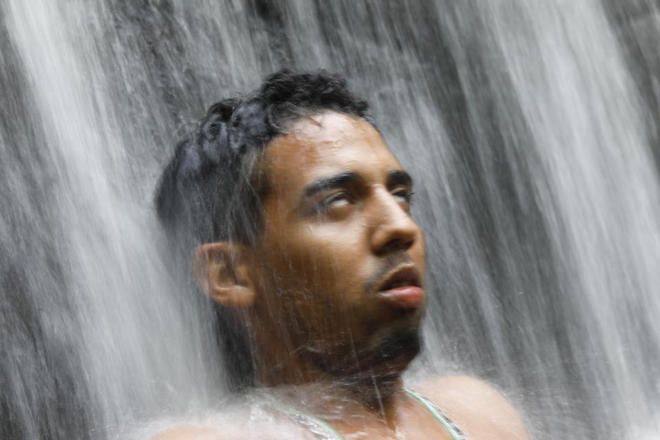 In this photo taken Oct. 12, 2019, a man with his eyes rolled back stands under a waterfall during a spiritual ceremony on Sorte Mountain where followers of indigenous goddess Maria Lionza gather annually in Venezuela's Yaracuy state. The tradition is hundreds of years old and draws on elements of the Afro-Caribbean religion Santeria and indigenous rituals, as well as Catholicism. (AP Photo/Ariana Cubillos)