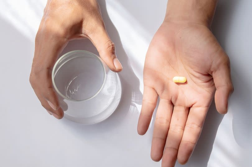 Asian man holding pills and glass of water isolated on white background. Health care and medicine concept