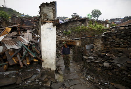 An earthquake victim, carrying wood recovered from a collapsed house, walks along a street near the debris of the collapsed houses at Barpak village at the epicenter of the April 25 earthquake in Gorkha district, Nepal, May 21, 2015. REUTERS/Navesh Chitrakar