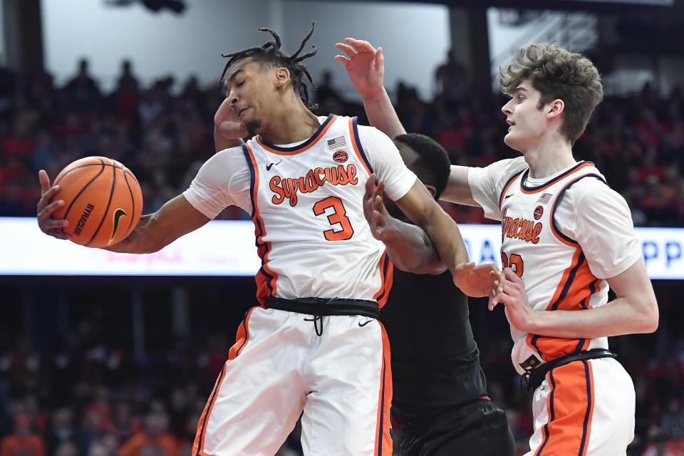 Syracuse guard Judah Mintz, left, grabs a rebound in front of center Peter Carey, right, and Louisville forward Brandon Huntley-Hatfield during the first half of an NCAA college basketball game in Syracuse, N.Y., Wednesday, Feb. 7, 2024. (AP Photo/Adrian Kraus)