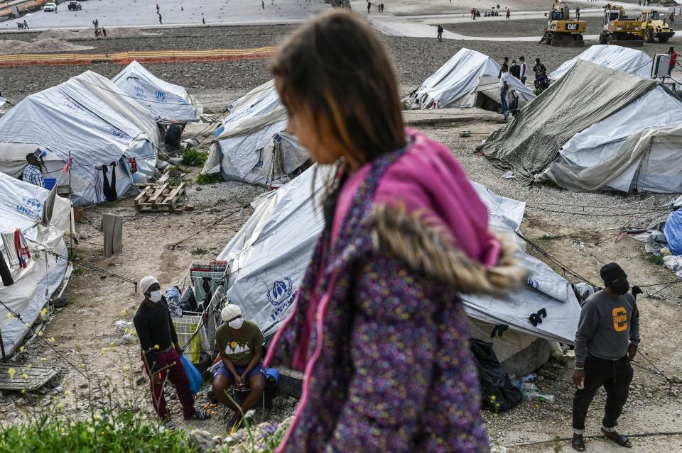 A child passes by migrants standing near tents inside the refugee camp of Kara Tepe in Mytilene, on Lesbos, on March 29, 2021. / Credit: ARIS MESSINIS/AFP via Getty Images