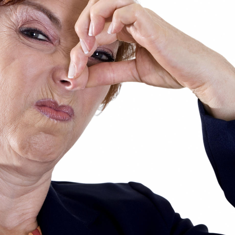 An older woman pinches her nose while making a disgusted facial expression